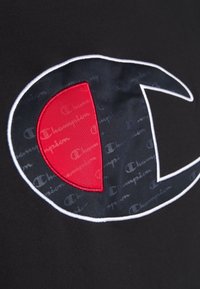 Tessuto nero con un logo Champion in evidenza caratterizzato da un design rosso e blu. Il logo presenta bordi bianchi e uno sfondo testurizzato.