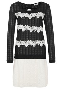 Robe en maille noire à manches longues avec trois bandes horizontales en dentelle fleurie blanche et une section jupe texturée en dentelle blanche.