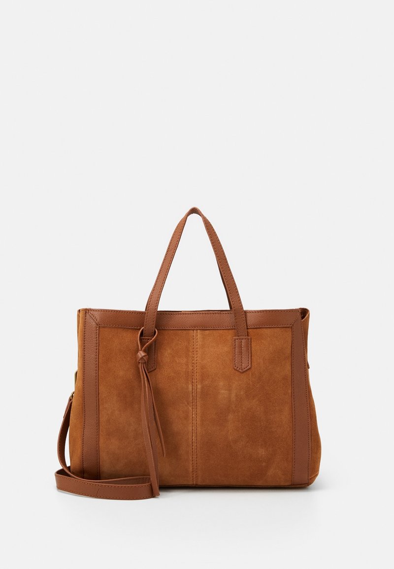 Sac fourre-tout en suède marron avec garniture en cuir, deux anses, une bandoulière amovible et un détail pompon en cuir sur l'anse.