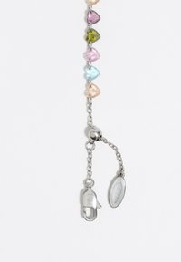 Perlas acrílicas coloridas en forma de hoja en rosa, azul, verde y púrpura, sobre una cadena de plata con un broche de langosta y una etiqueta ovalada.