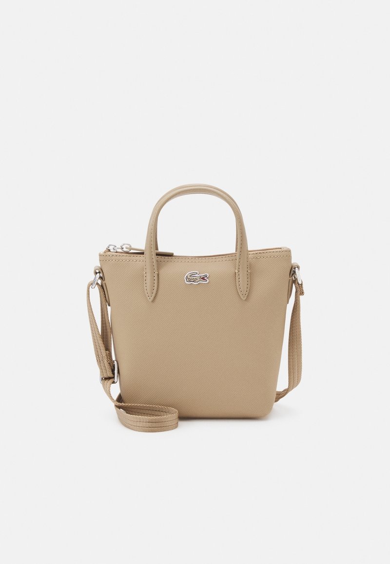 Sac à main beige en matériau synthétique texturé, doté d'une fermeture éclair supérieure, de deux poignées et d'une bandoulière amovible. Accent logo présent.