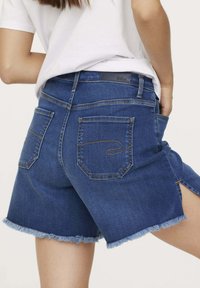 Shorts en denim bleu foncé avec poches arrière, coutures jaunes contrastantes et ourlet effiloché. Comprend une ceinture de marque avec un logo discret.