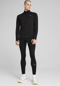 Zwart, lang mouw atletisch shirt met een halve rits kraag, gecombineerd met zwarte leggings en witte sneakers met kleurrijke accenten.