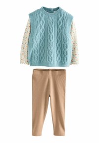 Ljusblå stickad väst med kabelmönster, lager-på-lager över en krämfärgad skjorta med färgglada prickar, tillsammans med beige ribbade leggings.