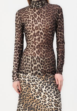 Femme portant un haut à col roulé à manches longues en tissu transparent à imprimé léopard et une jupe taille haute à imprimé léopard avec des motifs de couleurs différentes.