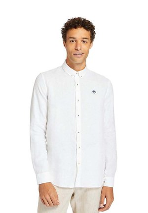 Camisa de botones blanca de manga larga hecha de lino, con un cuello y un pequeño logo azul en el pecho, que presenta una apariencia relajada y ligeramente texturizada.