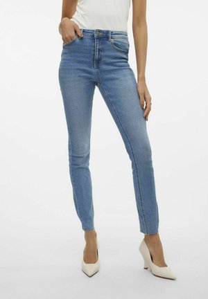 Blå højtaljede skinny jeans lavet af denim, med et klassisk fem-lomme design og frynset kant, parret med beige spidse hæle.