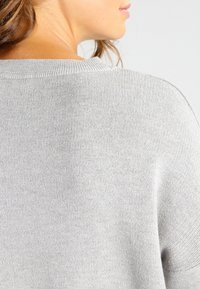 Ljust grå stickad tröja med ribbat mönster, som har en bred halsringning och en avslappnad passform. Tyget verkar mjukt och bekvämt.