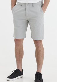 Shorts chino gris à devant plat, avec poches latérales et une couture soignée, associés à des baskets noires. Design décontracté avec un tissu léger.