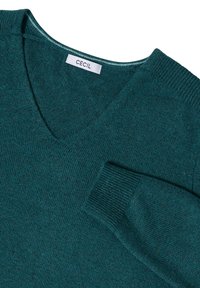 Suéter de pico en color verde azulado, hecho de una suave tela texturizada. Presenta puños y dobladillo acanalados, con una etiqueta situada debajo del escote.
