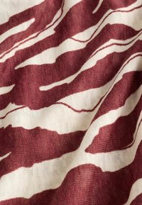 Tissu doux tricoté avec des rayures irrégulières de type zèbre en bordeaux et blanc, montrant la texture et des plis délicats.