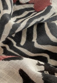 Kangas, millel on must-valge sebratriipude muster punaste aktsentidega, on valmistatud pehmest, tekstuuriga kangast, mis langeb voolavalt.