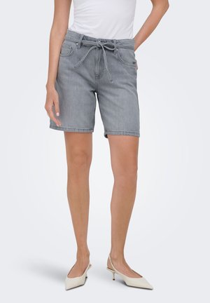 Vrouw draagt grijze denim shorts tot op de knie met voorzakken en een gestrikte tailleband, gecombineerd met witte puntige slingbackhakken.