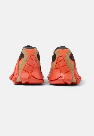 Oranssi ja beige urheilukengät, joissa on teksturoitu verkkomateriaali päälliosassa ja erottuva kumipohjan suunnittelu, jossa on jaettu kanta ja korostetut kaaret.
