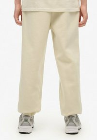Crème-kleurige, zachte joggerpants met een relaxed fit, voorzien van elastische boorden en bijpassende grijze sneakers met mesh-details.