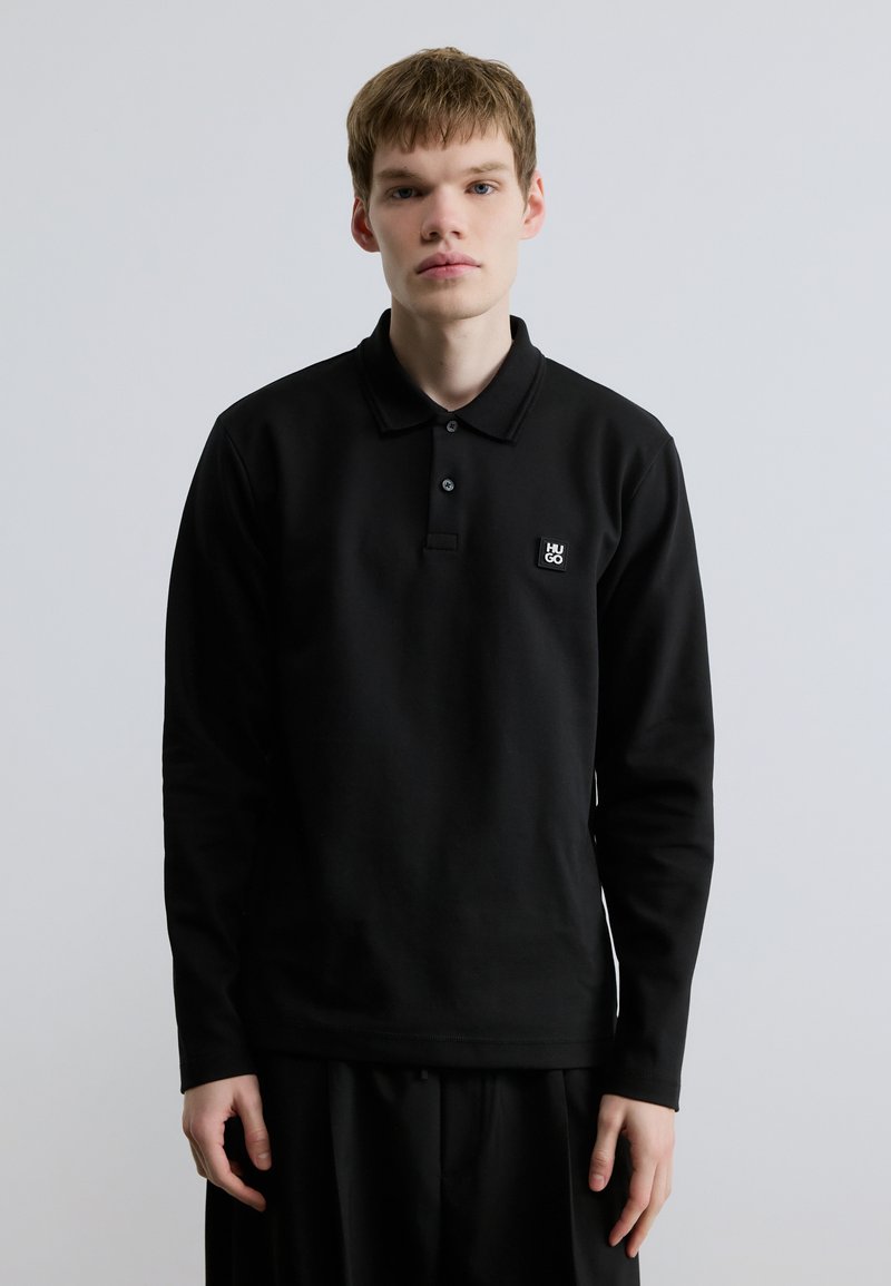 Μαύρο μακρυμάνικο πόλο μπλουζάκι με τρεις κουμπότρυπες, κατασκευασμένο από βαμβάκι. Διαθέτει μικρό ορθογώνιο λογότυπο της μάρκας στο στήθος.