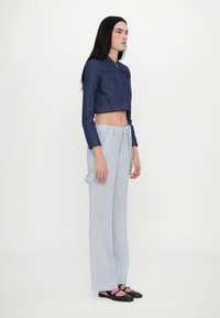 Kratka denim jakna z žepom v obliki srca, kombinirana s svetlo modrimi širokimi hlačami in rjavimi čevlji z roza trakovi.