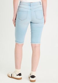 Bermuda shorts en denim bleu clair au design ajusté, dotés de quatre poches et de bords retroussés, associés à des baskets blanches et des chaussettes crème.