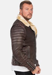 Giubbotto di pelle marrone con colletto in shearling, texture a coste, cerniere diagonali e dettagli trapuntati su spalle e lati.