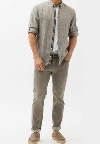 Camicia di lino grigia chiara con design a bottoni, maniche arrotolate, indossata sopra una maglietta bianca. Abbinata a pantaloni in denim grigi e scarpe slip-on beige.