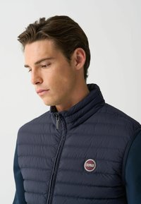 Navy quilted vest with high collar, zip closure, and Colmar logo patch. The fabric appears lightweight and smooth, with a slim fit design.