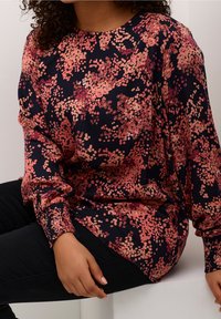 Blusa de manga larga en azul marino con un patrón de manchas en rosa y coral. Cuenta con un cuello redondo y puños fruncidos. Tejido suave.