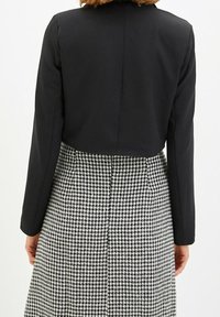 Czarna krótka marynarka z długimi rękawami, zestawiona z czarno-białą spódnicą w wzór hounds tooth. Gładki materiał, z czystymi szwami i klasycznym fasonem.