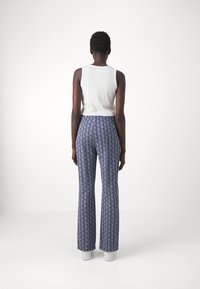 White sleeveless top paired with patterned blue flared pants featuring a geometric design and contrasting side stripes.