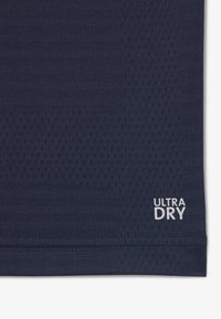 Tela texturizada azul oscuro con patrón de malla transpirable y etiqueta "ULTRA DRY" impresa en blanco cerca del dobladillo.