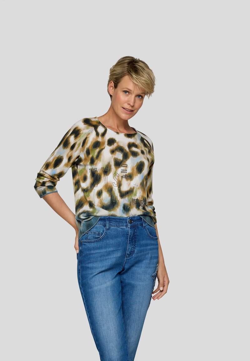Leopardenmuster-Pullover in Grüntönen und Creme, mit Rundhalsausschnitt und Dreiviertelärmeln, kombiniert mit blauen Jeans.