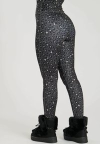 Black leopard print leggings with a shiny finish, featuring a high waist and visible seams. Paired with black fur-lined ankle boots.