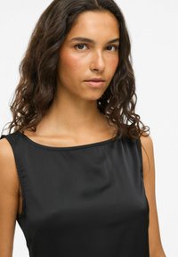 Haut sans manches noir avec une texture lisse et soyeuse et un décolleté large. Le design présente des lignes épurées et une silhouette ajustée.