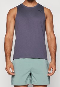 Débardeur de sport sans manches en tissu doux de couleur violette, avec un col rond et un logo noir subtil en haut à gauche.