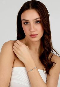 Braccialetto d'argento con tre pietre blu, caratterizzato da un design a catena delicata. Modella che lo indossa al polso su uno sfondo chiaro.