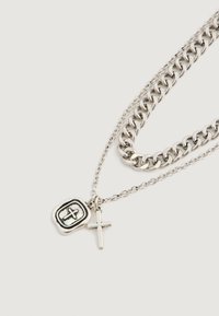 Kaks hõbedast kaelakeed heledal taustal; üks kett on paks ja teine õhuke, mõlemal ristripats, üks vaha pitsati disainiga.