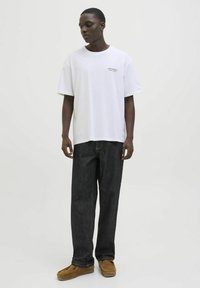 Hvid bomulds t-shirt med korte ærmer, prydet med grøn tekst. Kombineret med mørkeblå jeans og brune mokkasiner. Enkel design, afslappet pasform.
