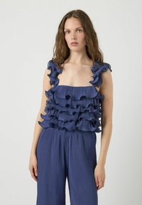 Marineblauw top met gelaagde ruches van lichtgewicht stof. Vierkante halslijn en brede banden, gecombineerd met geplooide marineblauwe broek.