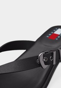 Μαύρο σανδάλι με λεπτό δερμάτινο λουρί και ασημένια αγκράφα, με λογότυπο Tommy Hilfiger στη σόλα.