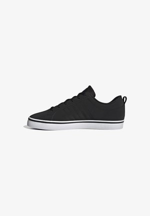 Zapatilla negra de corte bajo con cordones delanteros, sutiles rayas laterales y suela de goma blanca con detalle de línea negra, mostrada de perfil lateral.
