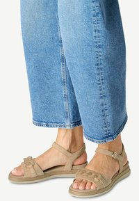 Beige Wildledersandalen mit einem breiten, geflochtenen Design und dekorativen Kettenakzenten. Niedriger Wedge-Absatz und verstellbarer Knöchelriemen für eine optimale Passform.