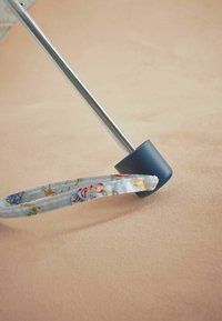 A silver metal cane with a blue rubber base and a patterned fabric grip featuring animals and anchors. Background is a soft, light pink.