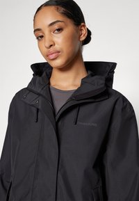 Schwarze wasserdichte Jacke mit abnehmbarem Kapuze, Frontreißverschluss und Taschen. Besitzt ein mattes Finish und ein dezentes Logo auf der Brust.