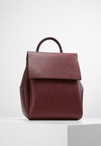 Sac à dos en cuir bordeaux au design structuré, forme rectangulaire, avec une poignée supérieure. Doté d'une fermeture à rabat et d'une texture lisse.