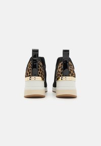 Sneakers neri con accenti leopardati, sposini neri lucidi, accessori dorati, suole bianche imbottite e suole in gomma marrone chiaro.