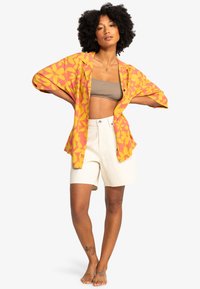 Floral print kimono in orange and yellow with wide sleeves, paired with beige cropped top and white high-waisted shorts. Smooth fabric texture.