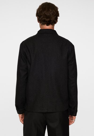 Svart texturerad jacka med krage, med en rak design och knappade ärmar. Visningen visar baksidan, utan synlig varumärkeslogotyp eller detaljer.