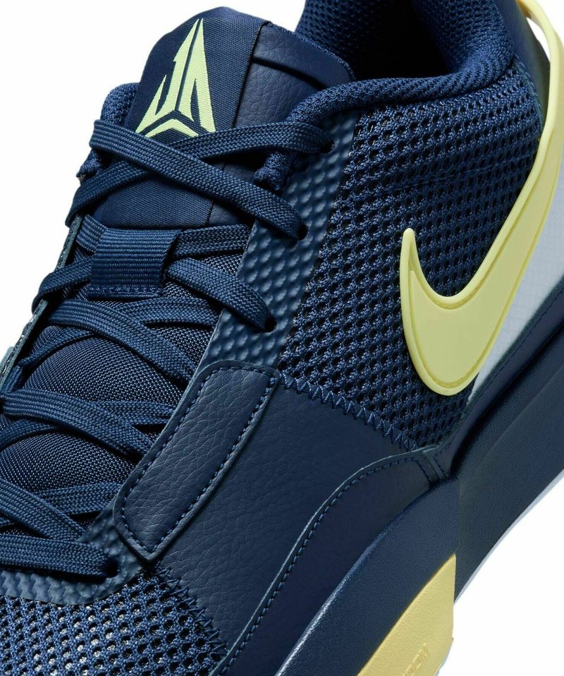 Granatowe trampki z siateczkową cholewką, skórzanymi akcentami, żółtym logo w kształcie łyżwy oraz smukłym designem z teksturowanymi powierzchniami.