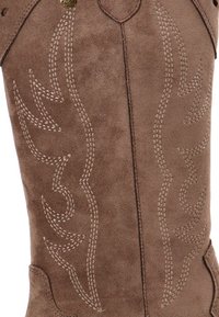 Caña de bota vaquera de ante marrón con costuras decorativas en beige claro en patrones similares a llamas.
