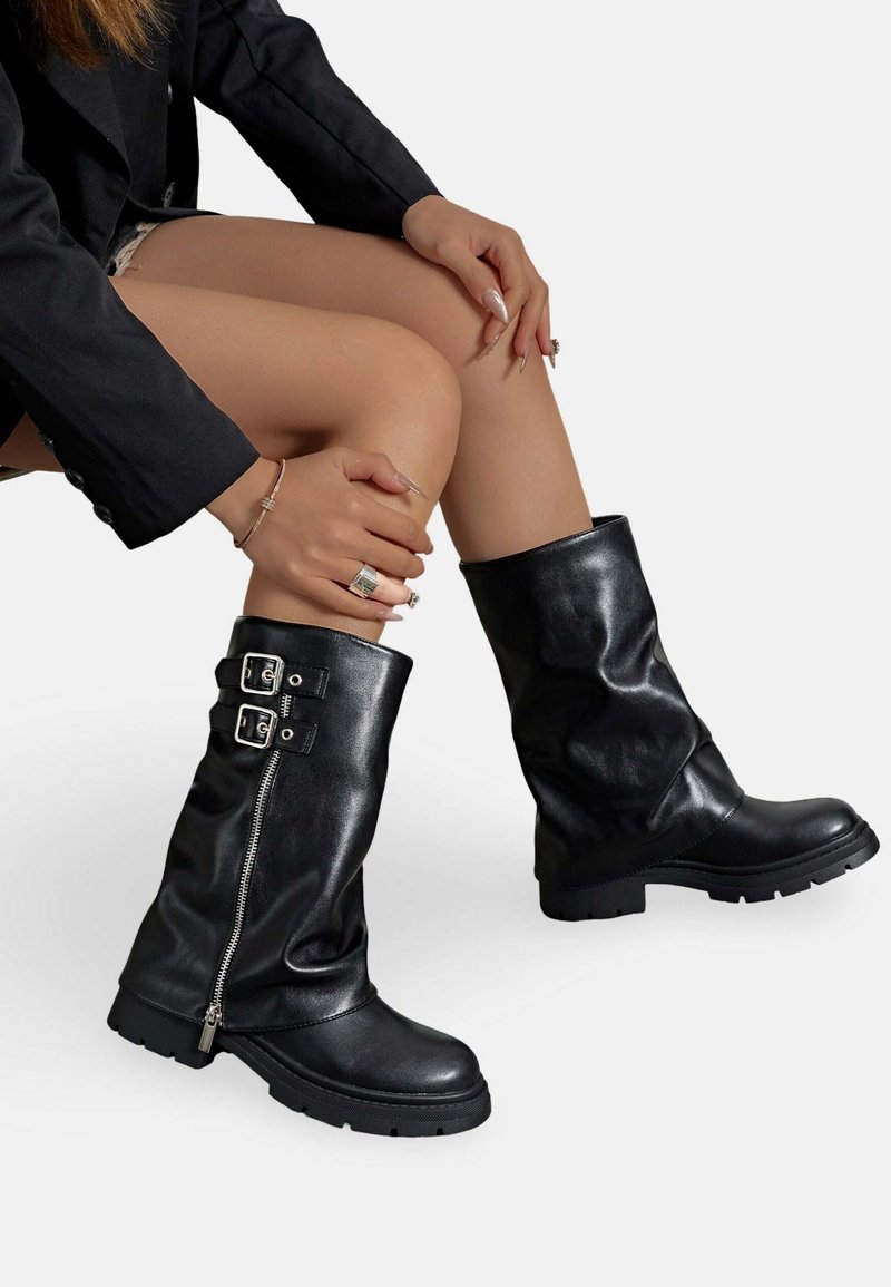 Bottes noires en cuir jusqu'au genou avec un design décontracté, des accents de double boucle en argent et une fermeture éclair sur le côté, dotées d'une semelle en caoutchouc texturée.