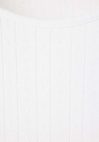 Tissu tricoté blanc avec des lignes verticales et de petits motifs décoratifs en forme de losange dans un motif répétitif.